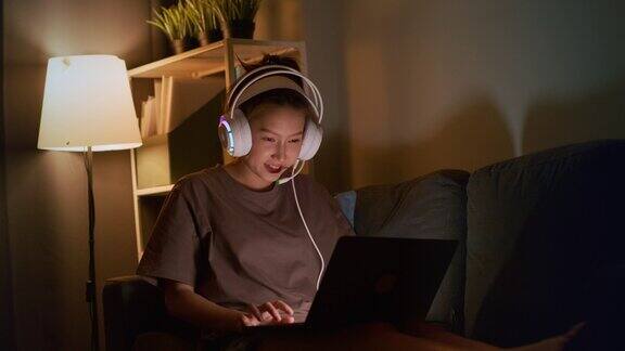 戴着耳机的年轻亚洲女子正在家里玩网络游戏