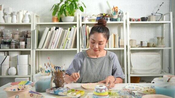 4K亚洲妇女喜欢在陶器作坊工作室画自制的陶器盘子