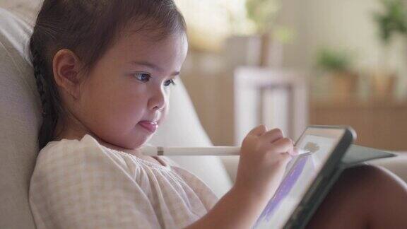 小女孩坐在沙发上喜欢用电子笔在平板上画画