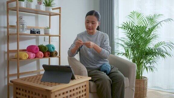 亚洲妇女教如何钩针编织在线视频剪辑在平板电脑坐在家里的客厅