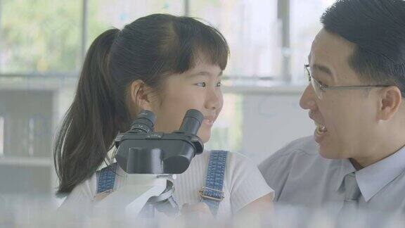 亚洲男科学家在教室实验室用显微镜教小女孩科学实验人具有科教观念