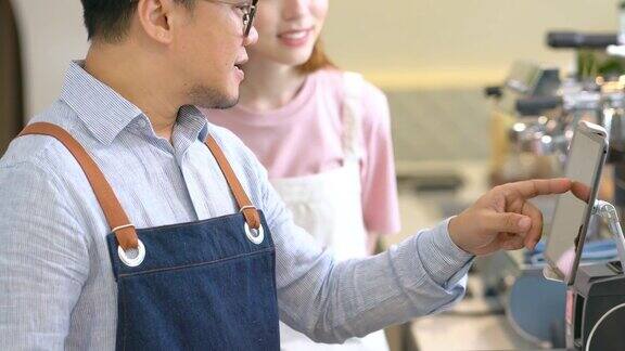 4K亚洲男咖啡店老板教年轻女服务员使用数字平板电脑