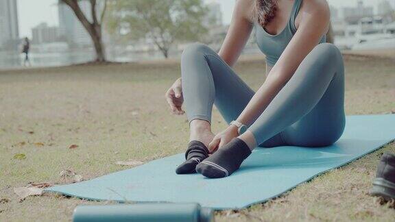 年轻的亚洲女性在公园练习瑜伽后穿上袜子自我照顾积极健康的生活方式