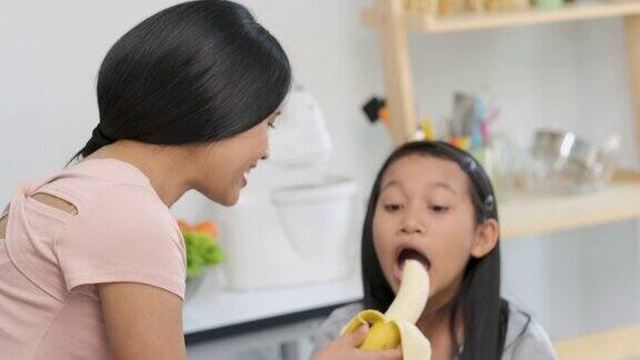 慢镜头亚洲母亲在厨房给女儿喂香蕉