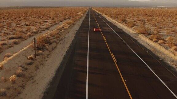 鸟瞰图红色经典车沿着荒凉的沙漠道路在日落