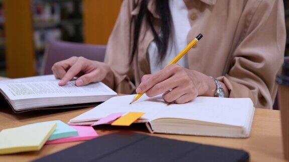 亚洲女学生坐在图书馆里准备考试在笔记本上做笔记准备大学考试在大学图书馆里严肃地寻找信息