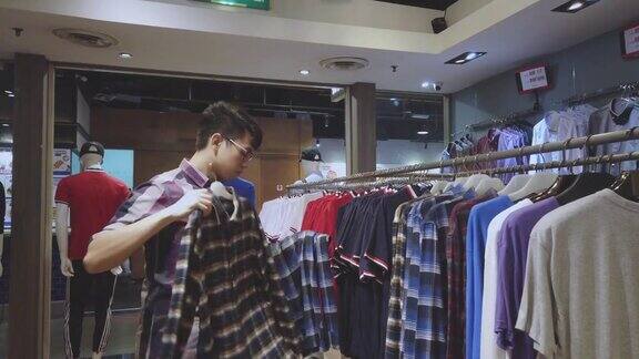 亚洲华人男性手拿男装衬衫在服装店选择正确的一件购物