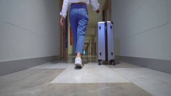 一位女士走在酒店的走廊上用轮子推着行李箱