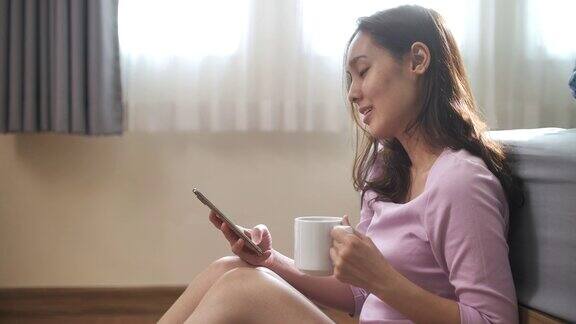 在卧室里用智能手机喝咖啡吃早餐的亚洲女人