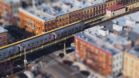 在阳光明媚的一天火车驶过纽约布鲁克林默特尔大道的地铁高架线无人机视频倾斜移位效果与前平移摄像机运动跟随火车