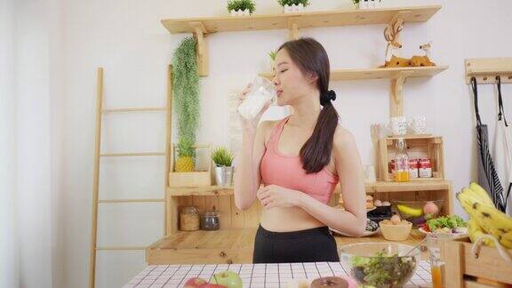 注重健康的亚洲女性穿着运动服站在厨房喝牛奶