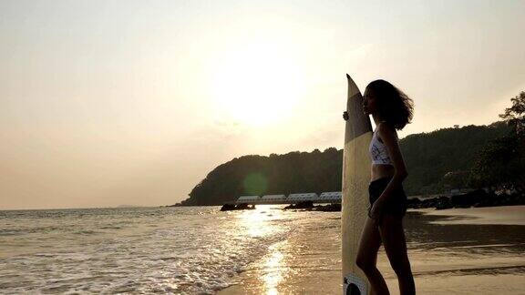日落时分冲浪女孩站在热带海滩上冲浪板的剪影