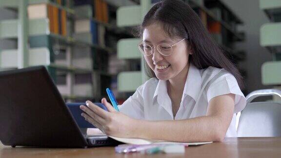 亚洲女大学生在公共图书馆看书用笔记本电脑和智能手机做作业