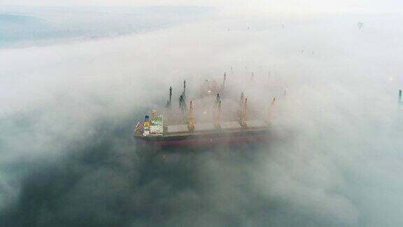 在保加利亚瓦尔纳海港无人机拍摄的大雾中的货船和工业起重机