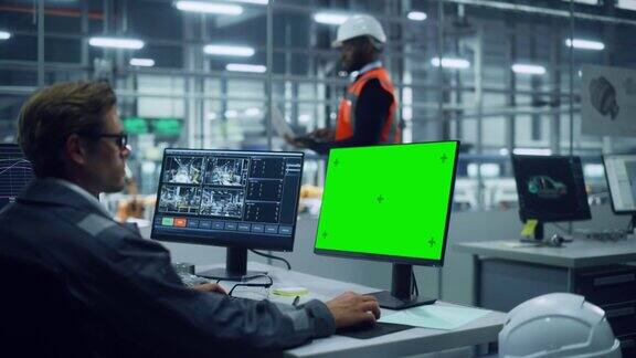 非裔美国工程师在汽车装配厂使用笔记本电脑和向外看汽车工厂生产线操作员在电脑绿色屏幕显示的桌子上工作