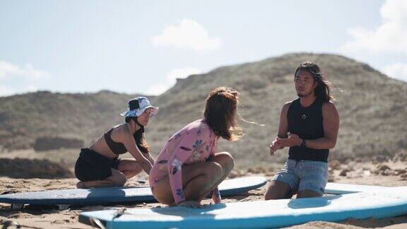 亚裔华人冲浪男教练在沙滩上指导女学生在海上冲浪