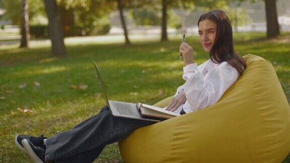 专注的年轻女子坐在公园的豆袋椅上看着笔记本电脑研究一个新程序在网上做一个研究项目做一个远程工作任务