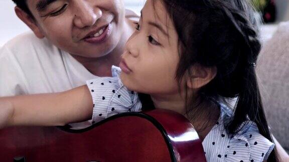 父亲教孩子们弹吉他亚洲男人和孩子一起坐在客厅的沙发上学习弹吉他脸部特写