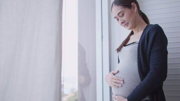 幸福的亚洲孕妇站在家里望着窗外
