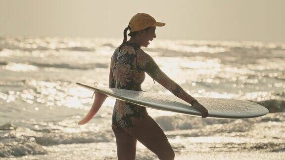 日落时分女冲浪者带着冲浪板在海滩上散步慢动作