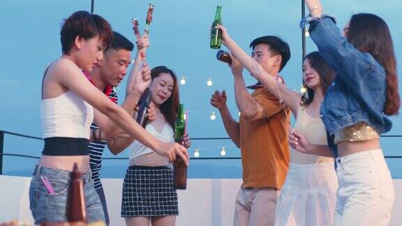 一群年轻的亚洲人在日落时分和朋友们一起享受拿着啤酒瓶在屋顶派对上跳舞