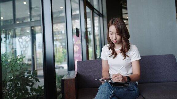 年轻的成年人快乐微笑的亚洲学生在线学习在网上聊天在网上聊天会议使用平板电脑在咖啡馆或办公室大学学院女生远程学习