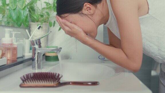 上午晚些时候年轻的亚洲女人在家里的厕所里对着镜子用泡沫洗脸日常的生活方式