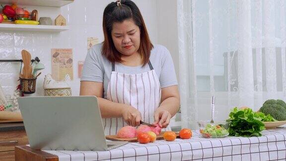 亚洲孕妇在厨房里从网上学习如何做健康的饭菜胖女人准备蔬菜沙拉作为减肥食品健康饮食
