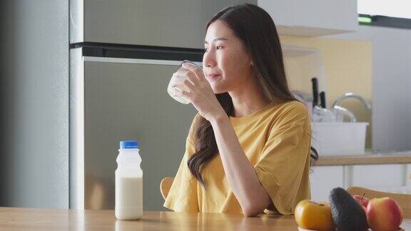 年轻的亚洲妇女在家里的厨房喝牛奶健康的生活方式