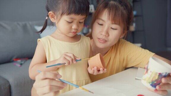 快乐快乐的亚洲家庭妈妈教学步的小女孩在家里客厅的桌子上画画玩得开心放松