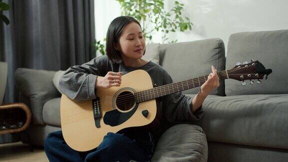 亚洲女孩在家里弹奏原声吉他乐器坐在地板上