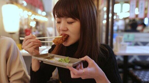 一个年轻的日本女人在居酒屋酒吧吃炸鸡
