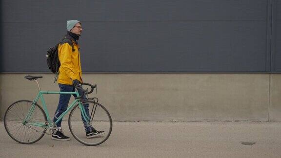 侧视图的白人男子在黄色夹克推动他的自行车通勤