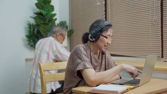 资深夫妇亚洲成熟与耳机使用笔记本电脑在家里工作