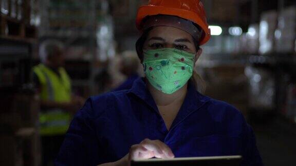 中年妇女的肖像戴着口罩使用数字平板电脑-工作在仓库工业