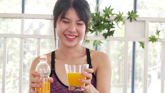 妇女双手捧着冰凉的橙汁新鲜水果清凉饮用亚洲女性笑笑看着镜头健康护理家庭健身生活方式美丽的女性从鸡尾酒瓶中倒橙汁
