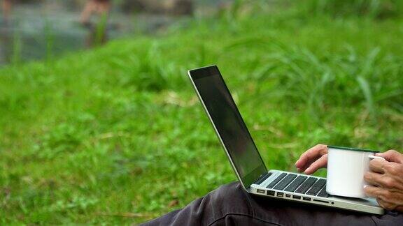 亚洲男子在公园露营度假时使用笔记本电脑