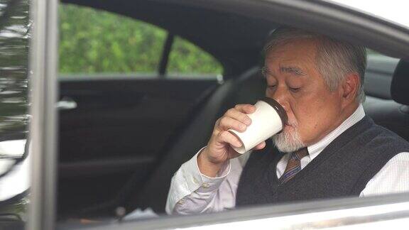 4K亚洲资深商人坐在车后座喝着热咖啡