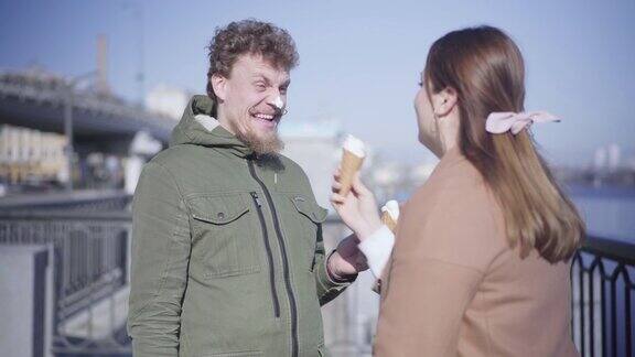 快乐的年轻女子用冰淇淋摸着男子的鼻子大笑正面的白人夫妇在阳光明媚的秋日户外约会肖像幸福生活方式团结欢乐