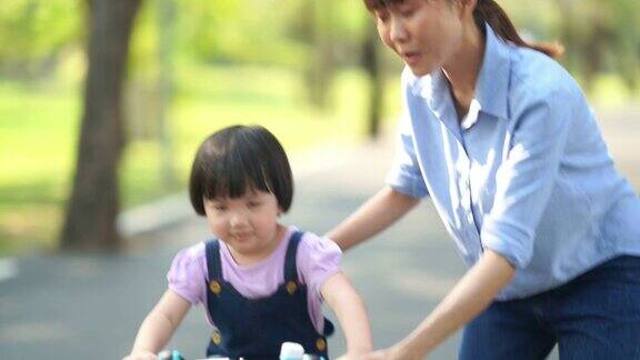 亚洲小女孩和年轻的老师在花园里骑自行车