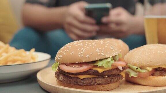 桌上汉堡包的4k视频在家沙发上用智能手机的年轻人不健康的生活理念