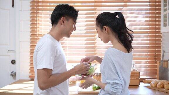 年轻漂亮的亚洲夫妇在家里的厨房里做健康的食物边说边笑