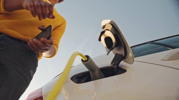 非洲年轻人将电动汽车插头插入汽车充电的低角度视图