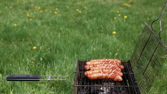 美味的烧烤在绿草地的背景热狗香肠在户外烧烤盘上煎炸野餐时用烧烤架烤食物