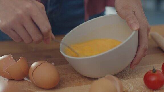 年轻的亚洲女厨师把鸡蛋搅拌到陶瓷碗里在厨房桌子上的木板上用蔬菜做煎蛋卷