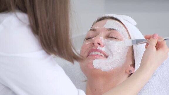 一位美容师正在用刷子给一位女士的脸上涂保湿面膜护肤理念
