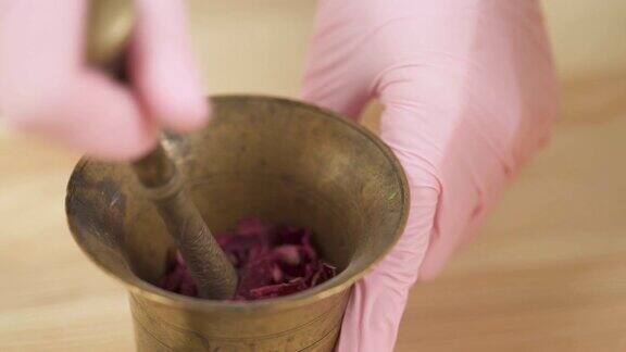 特写镜头一个女孩正在用杵将干燥的玫瑰花瓣磨成粉末