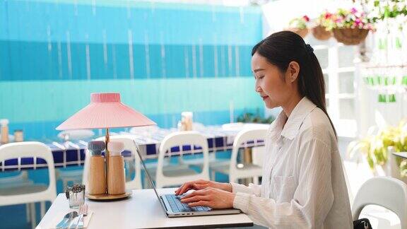 年轻的成年亚洲女性在办公室外的咖啡店使用笔记本电脑工作