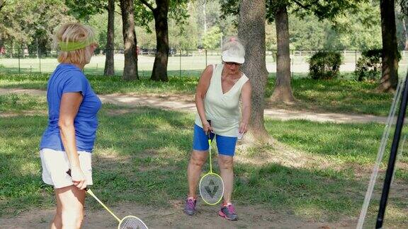 两名老年妇女拿着球拍打羽毛球