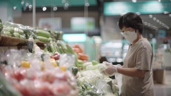 戴着防护口罩的女子在超市挑选蔬菜